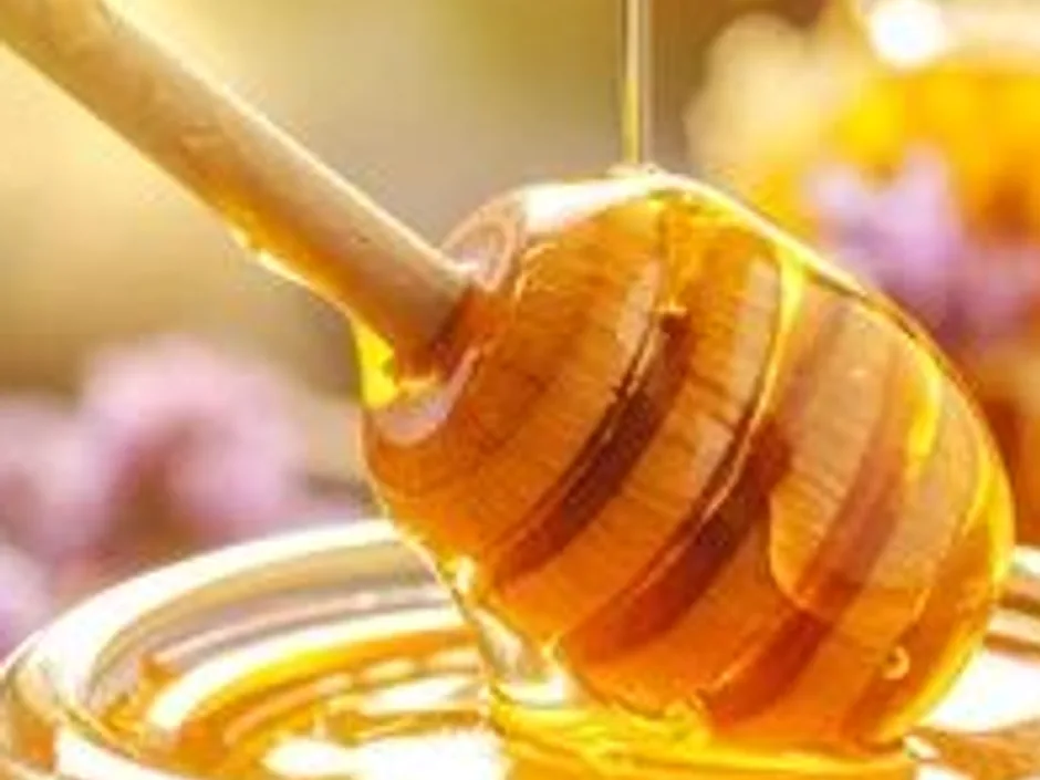An open glass jar of golden honey with a wooden dipper resting in it.